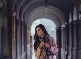 Les écharpes en soie pour un look raffiné woman holding scarf with cross legs in between of gray concrete wall