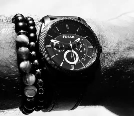 person wearing round Fossil chronograph watch with link band displaying 01:47 time