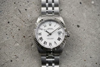 Rolex Datejust 36 posée sur béton brossé, cadran blanc avec chiffres romains et bracelet jubilé en acier inoxydable